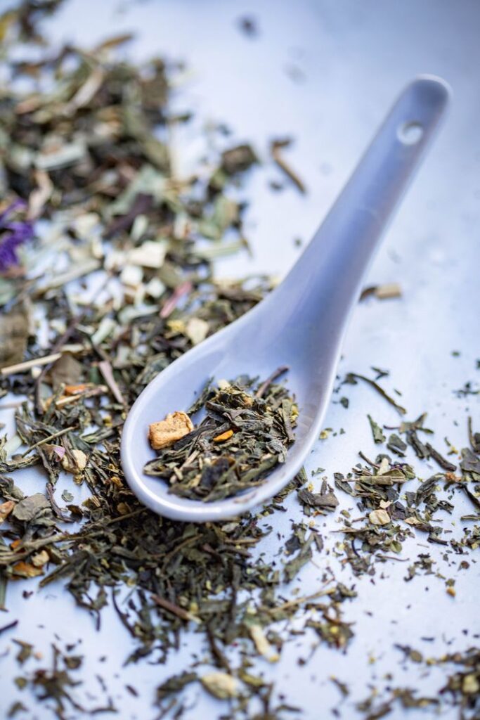 A vertical close-up of a Chinese spoon filled with assorted dried herbs on a scattered background.