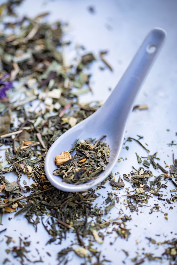 A vertical close-up of a Chinese spoon filled with assorted dried herbs on a scattered background.