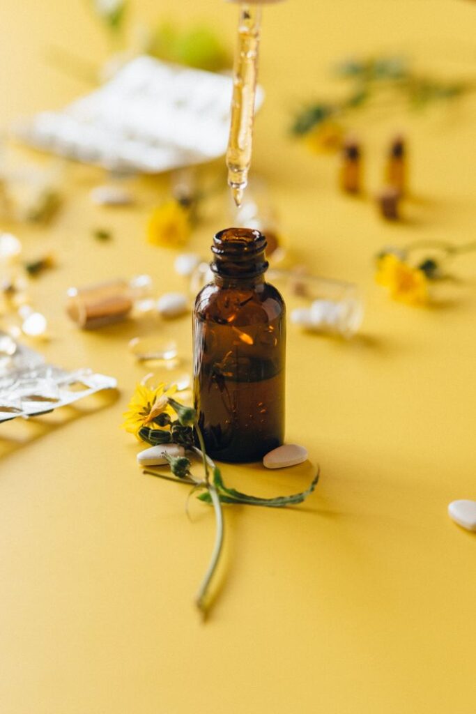 Brown glass bottle with dropper and yellow flowers on a yellow surface.