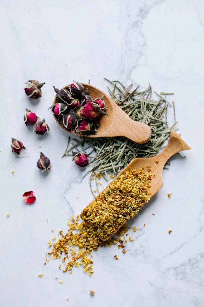 Flat lay of dried rosebuds, rosemary, and chamomile on a marble surface.